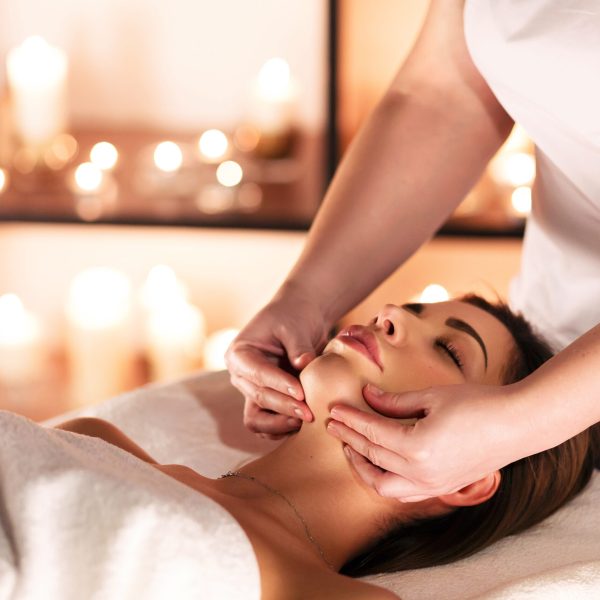 Hands of female masseuse doing a massage on the chin of a beautiful young woman lying on a massage table with closed eyes in a spa salon
