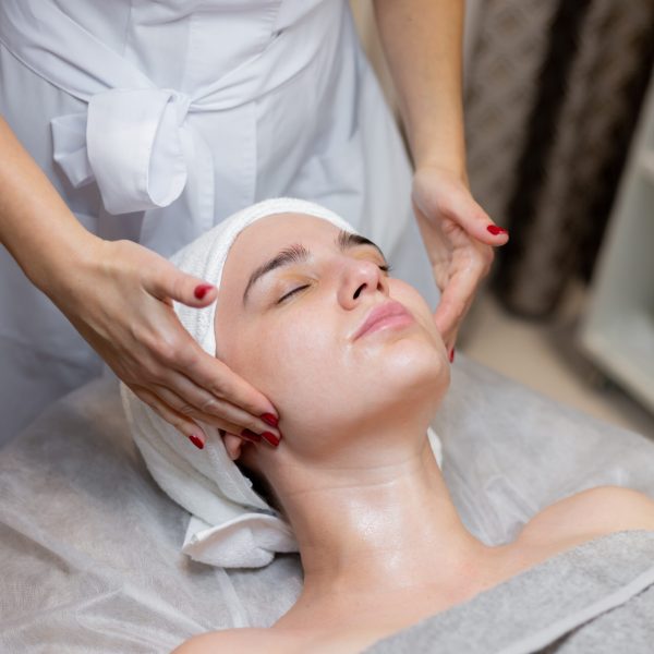 A young beautiful girl lies on the beautician's table and receives procedures, a light facial massage using oil. Woman takes care of herself, enjoys massage